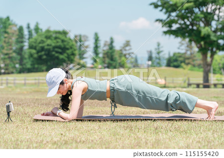 A woman who does yoga and muscle training using a smartphone app and smart watch in the park (yoga mat) 115155420