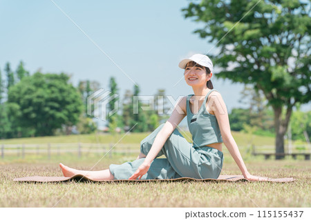 一個女人在公園裡用瑜伽墊做瑜伽、伸展和鍛煉 115155437