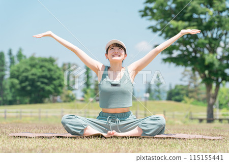 A woman doing yoga, stretching, deep breathing, and refreshing using a yoga mat in the park (sunny, weather) 115155441