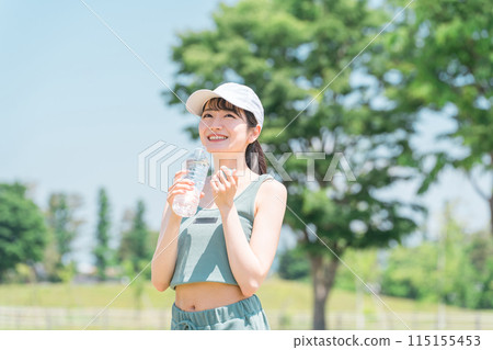 A woman drinking water/mineral water while exercising (hydration, exercise, workout, running, walking) 115155453