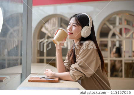 A relaxed Asian woman is daydreaming while sipping coffee and listening to music in a cafe. 115157036