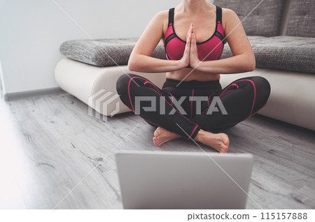Fit young woman in sportswear practicing doing yoga exercises and watching videos online tutorials on laptop, training in living room during quarantine and closed gyms. 115157888