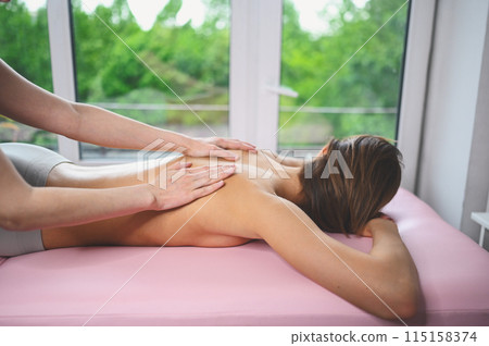 Young beautiful unrecognizable woman lying on massage table and enjoying back therapeutic massage. Close-up hands of a massage therapist masseur massaging female spine in spa. Body care concept. Young beautiful unrecognizable woman lying on massage table and enjoying back therapeutic massage. Close-up hands of a massage therapist masseur massaging female spine in spa. Body care concept. 115158374