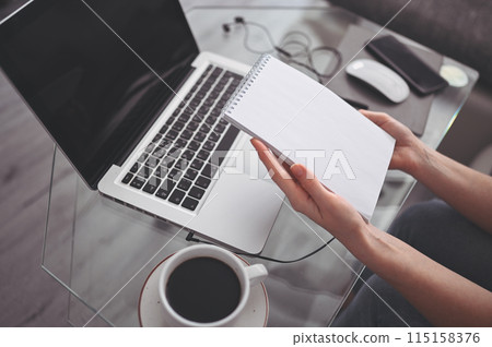 Unrecognizable woman hands writing in empty mock up notebook and computer. Freelancer using smart phone and laptop at home during quarantine. 115158376
