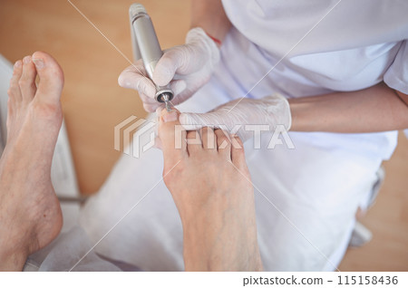 Hardware medical pedicure with nail file drill apparatus. Patient on pedicure treatment with pediatrician chiropodist. Foot peeling treatment at spa with a special device. Clinic of Podiatry Podology 115158436