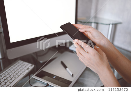 Female hands using smart phone in interior workplace, freelance business woman using cell phone at office desk, working from home using smart phone and notebook computer. Female hands using smart phone in interior workplace, freelance business woman using cell phone at office desk, working from home using smart phone and notebook computer. 115158470