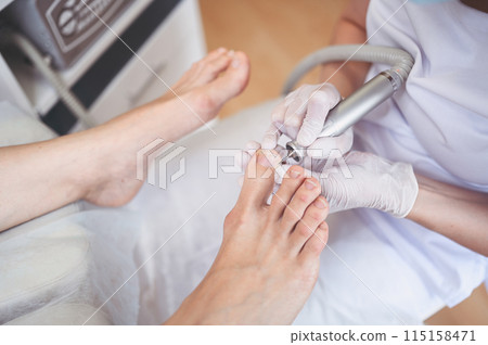 Hardware medical pedicure with nail file drill apparatus. Patient on pedicure treatment with pediatrician chiropodist. Foot peeling treatment at spa with a special device. Clinic of Podiatry Podology Hardware medical pedicure with nail file drill apparatus. Patient on pedicure treatment with pediatrician chiropodist. Foot peeling treatment at spa with a special device. Clinic of Podiatry Podology 115158471