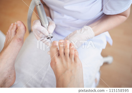 Hardware medical pedicure with nail file drill apparatus. Patient on pedicure treatment with pediatrician chiropodist. Foot peeling treatment at spa with a special device. Clinic of Podiatry Podology 115158595