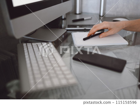 Unrecognizable woman hands writing in empty mock up notebook and computer. Freelancer using smart phone and laptop at home during quarantine. 115158596