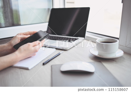 Female hands using smart phone in interior workplace, freelance business woman using cell phone at office desk, working from home using smart phone and notebook computer. Female hands using smart phone in interior workplace, freelance business woman using cell phone at office desk, working from home using smart phone and notebook computer. 115158607