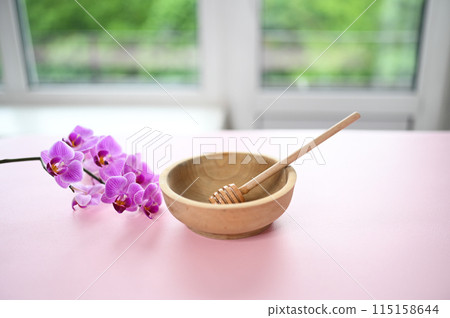 Set of depilation and beauty on pink background concept - sugar paste or hair removal waxing melted paste, orchid and female hands. Sugar paste or honey in a wooden bowl with a special dipper stick. 115158644