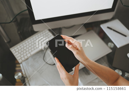Female hands using smart phone in interior workplace, freelance business woman using cell phone at office desk, working from home using smart phone and notebook computer. 115158661