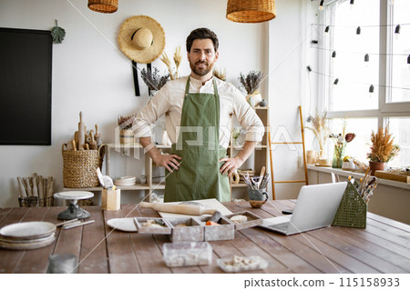 Portrait of male potter, standing in front of table with tools for sculpture. 115158933