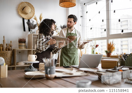 Saleswoman typing on digital tablet while bearded seller holding ceramic bowl. 115158941