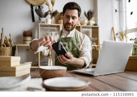 Mature man, potter, engaged in making home-made dishes and updating website. Mature man, potter, engaged in making home-made dishes and updating website. 115158993