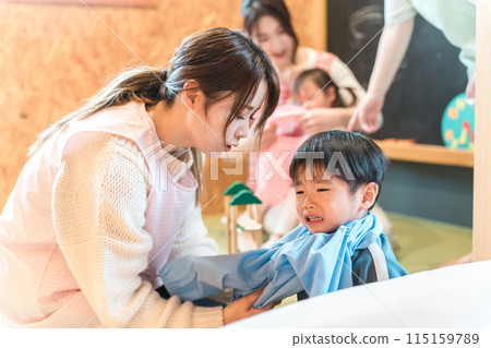 A female nursery teacher changing clothes at a nursery school and a boy who is going through the "no" phase 115159789