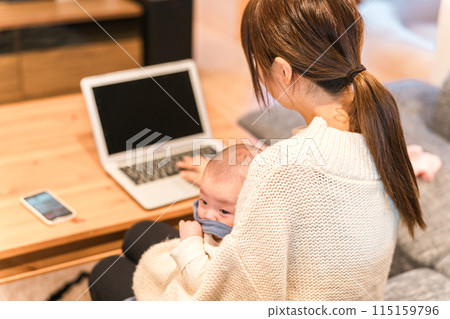 A young Asian woman working remotely while raising a child or holding a baby 115159796