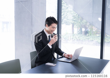 一名男子在時尚的辦公室裡一邊喝著咖啡,一邊看著電腦,微笑著在線上交流。 一名男子在時尚的辦公室裡一邊喝著咖啡,一邊看著電腦,微笑著在線上交流。 115160116