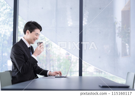 一名男子在時尚的辦公室裡一邊喝著咖啡,一邊看著電腦,微笑著在線上交流。 一名男子在時尚的辦公室裡一邊喝著咖啡,一邊看著電腦,微笑著在線上交流。 115160117