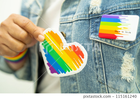 Asian lady wearing rainbow flag wristbands and hold red heart, symbol of LGBT pride month celebrate annual in June social of gay, lesbian, bisexual, transgender, human rights. 115161240