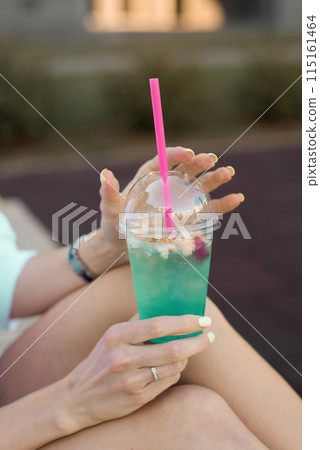 Refreshing non-alcoholic cocktail in a plastic cup with a straw in the hands of a woman 115161464