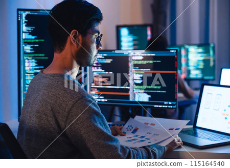 Asian software developers working on multiple screens displaying code and application diagrams at night in modern office Asian software developers working on multiple screens displaying code and application diagrams at night in modern office 115164540