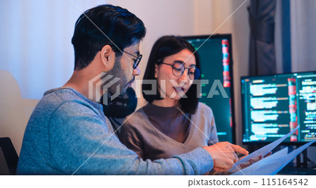 Asian software developers teams working on multiple screens displaying code and application diagrams at night in modern office 115164542