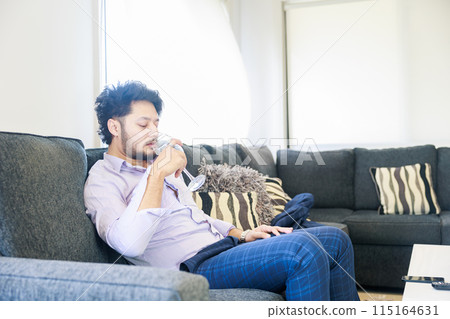 A foreign man sitting on a sofa and drinking wine 115164631