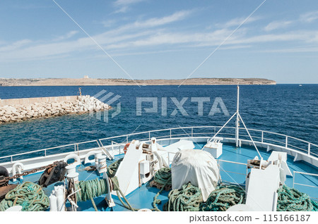 The boat sails from the island into the sea leaving waves on the water 115166187