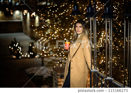 beautiful young girl in a beige coat with a paper glass of coffee against the backdrop of many bokeh lights beautiful young girl in a beige coat with a paper glass of coffee against the backdrop of many bokeh lights 115166273