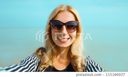 Summer portrait of happy smiling young woman taking selfie on smartphone on the beach on sea 115166937