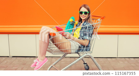 Modern stylish young woman using digital tablet computer in shopping trolley cart on city street 115167355