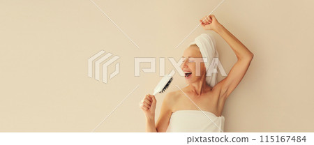 Happy cheerful woman having fun sings with hair comb after shower drying her wet hair with towel Happy cheerful woman having fun sings with hair comb after shower drying her wet hair with towel 115167484