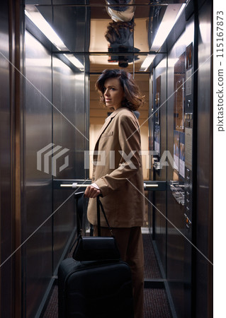 Young businesswoman with luggage bags riding in hotel elevator Young businesswoman with luggage bags riding in hotel elevator 115167873