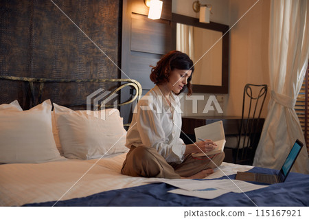Busy young businesswoman working online from hotel room 115167921