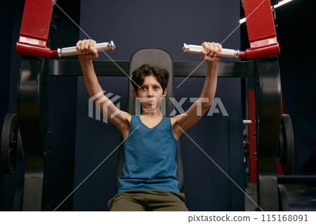 Active athletic preteen boy training arms muscles at gym 115168091
