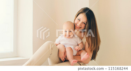 Happy smiling young mother playing with baby in white room at home 115168244
