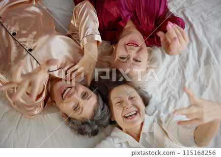 Top view on smiling elderly woman friends wearing pajamas lying in bed 115168256