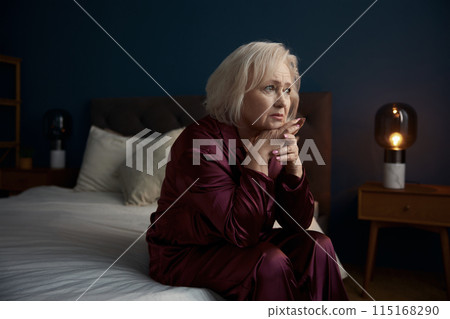 Sad elderly woman wearing pajamas sitting on bed feeling loneliness 115168290