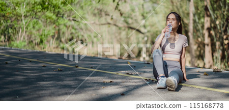 Young woman in athletic wear sitting on roadside, drinking water after outdoor workout in a natural setting. Young woman in athletic wear sitting on roadside, drinking water after outdoor workout in a natural setting. 115168778