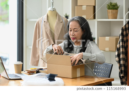 Smiling mature woman ecommerce business worker preparing clothes package at her shop 115168993