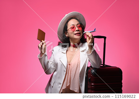Middle age woman in straw hat holding airplane model and passport on pink background 115169022