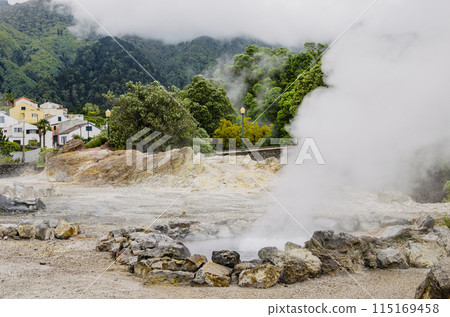 Smoke emanating from an active hot volcanic geyser against the background of green hills and a small village in the department Focus on a nearby geyser with steam Smoke emanating from an active hot volcanic geyser against the background of green hills and a small village in the department Focus on a nearby geyser with steam 115169458