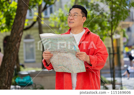 Asian man tourist exploring city street sightseeing holding paper map check direction searching way Asian man tourist exploring city street sightseeing holding paper map check direction searching way 115169606