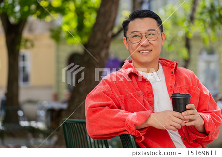 Happy Asian man enjoying drinking morning coffee hot drink, relaxing, taking a break on city street Happy Asian man enjoying drinking morning coffee hot drink, relaxing, taking a break on city street 115169611