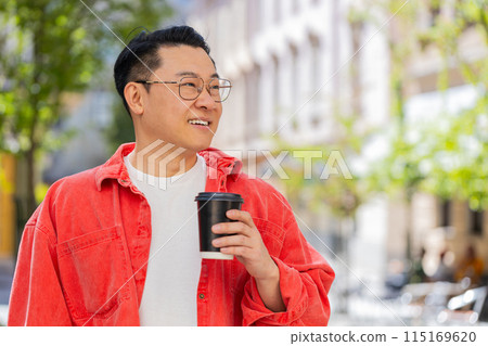 Happy Asian man enjoying drinking morning coffee hot drink, relaxing, taking a break on city street Happy Asian man enjoying drinking morning coffee hot drink, relaxing, taking a break on city street 115169620