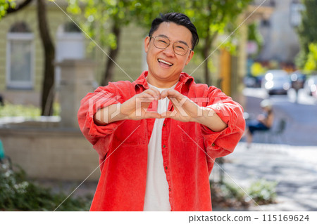 Asian man makes symbol of love, showing heart sign to camera, express romantic positive feelings 115169624