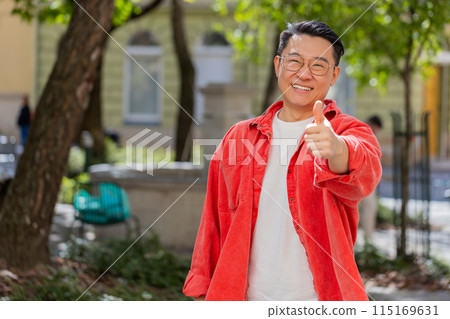 Happy Asian man showing thumbs up like sign positive something good positive feedback in city street 115169631