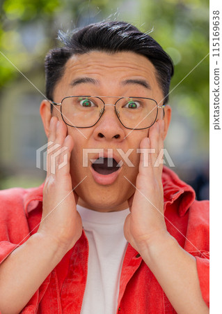 Asian man looking surprised at camera shocked by sudden win good victory news, wow in city street Asian man looking surprised at camera shocked by sudden win good victory news, wow in city street 115169638