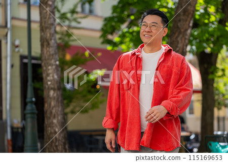 Happy smiling Asian middle-aged man tourist walking in urban city street outdoors in summer daytime Happy smiling Asian middle-aged man tourist walking in urban city street outdoors in summer daytime 115169653